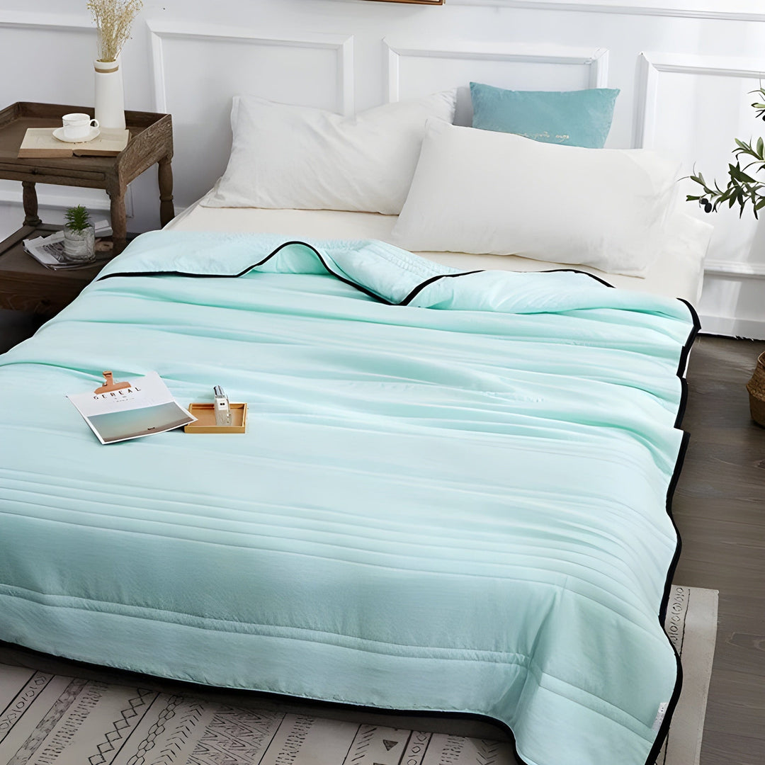 Aquamarine cooling sleep blanket laid out neatly on a bed with pillows
