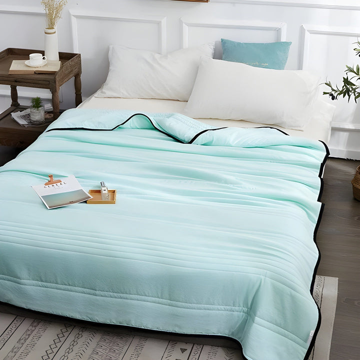 Aquamarine cooling sleep blanket laid out neatly on a bed with pillows