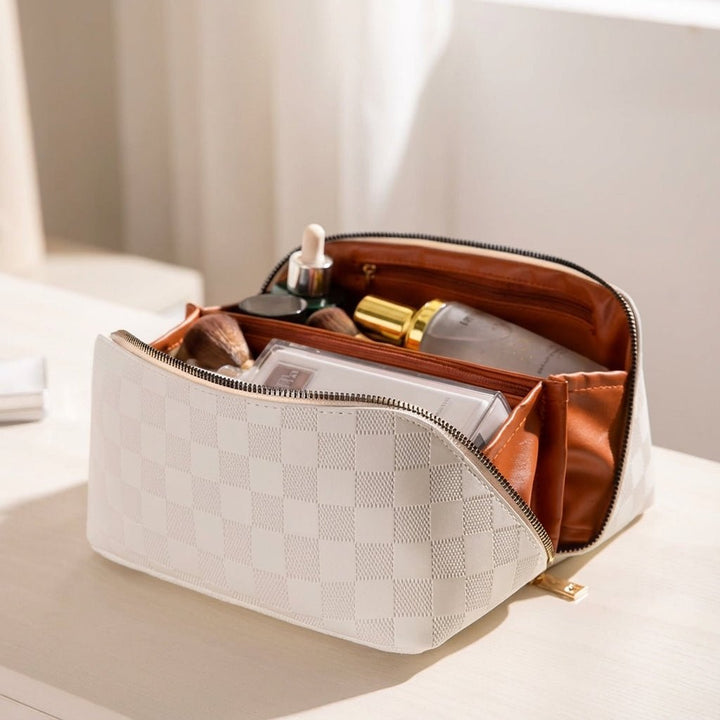 Cream cosmetic bag open on table showing interior compartments and stored makeup