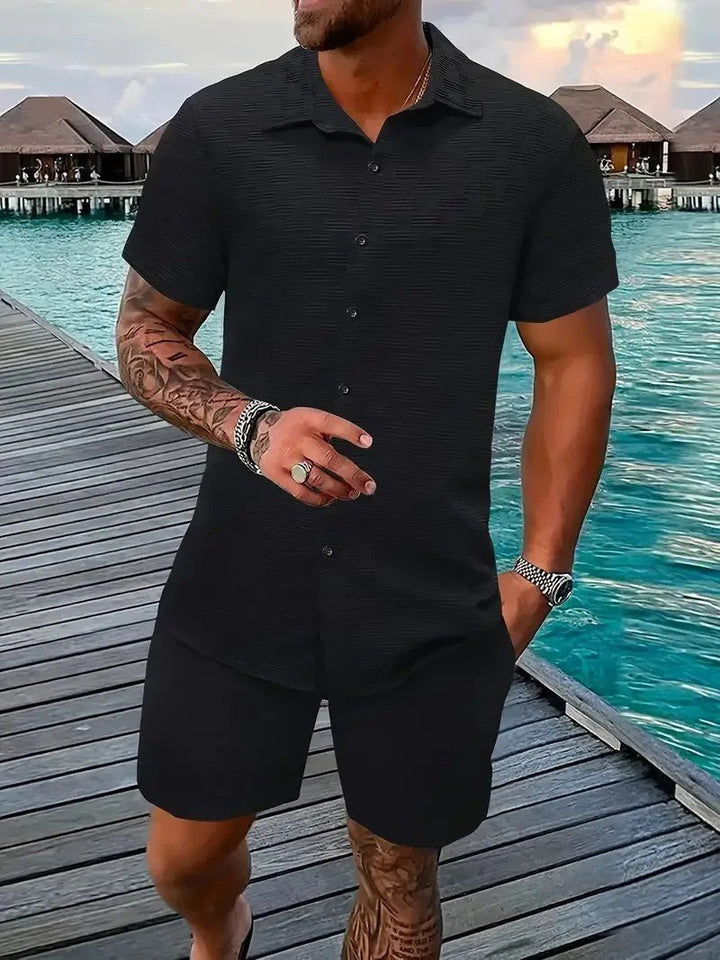Man wearing a black short-sleeve shirt and matching shorts set by the water