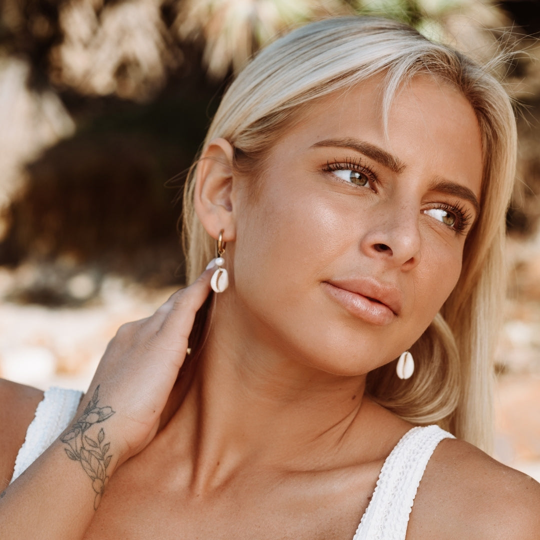 Woman wearing bohemian cowrie shell earrings in a sunny outdoor setting