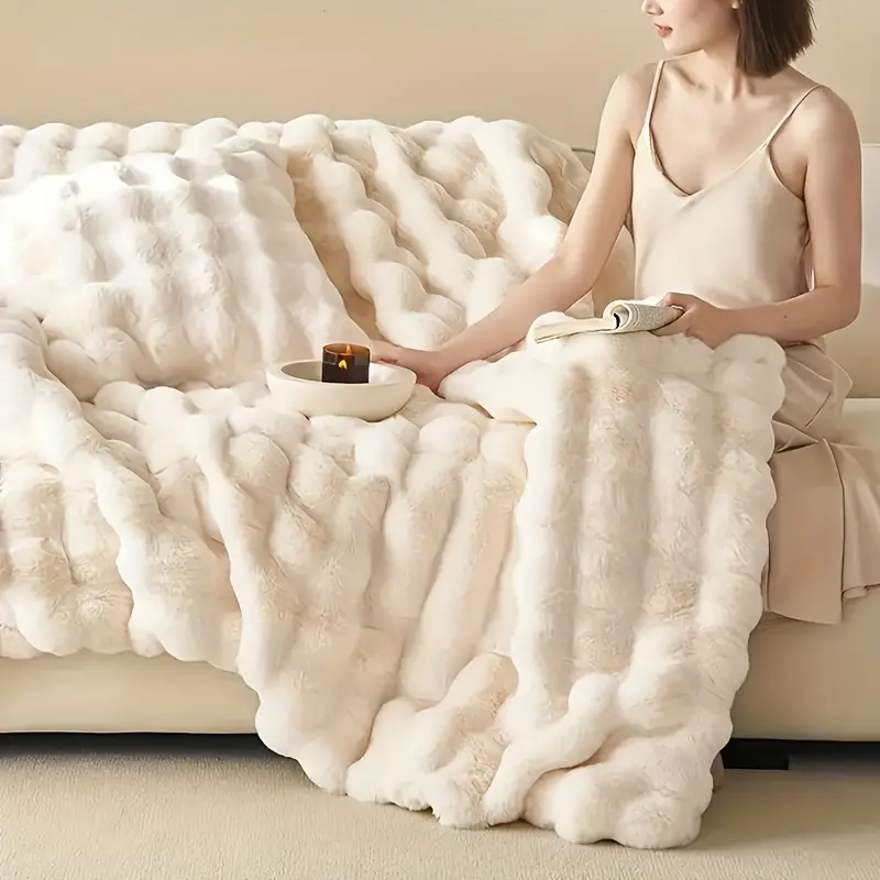 A woman relaxing on a beige sofa next to a white textured plush blanket