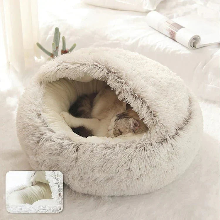 A fluffy beige calming nest bed with a cat resting peacefully inside on a white bed.