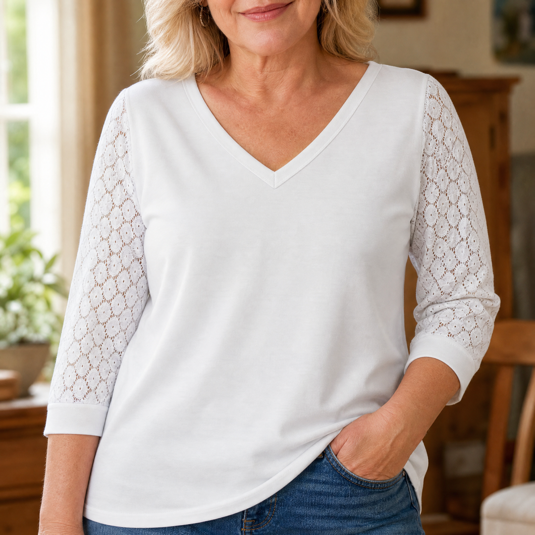 Close-up of a woman wearing a white V-neck top with honeycomb lace sleeves and blue jeans.