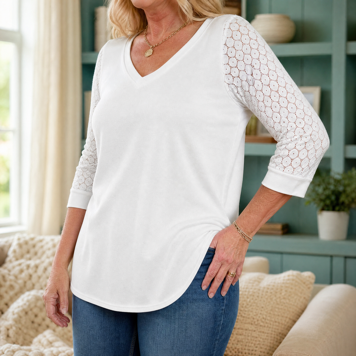 Full view of a woman wearing a white V-neck top with decorative sleeves and a curved hem.