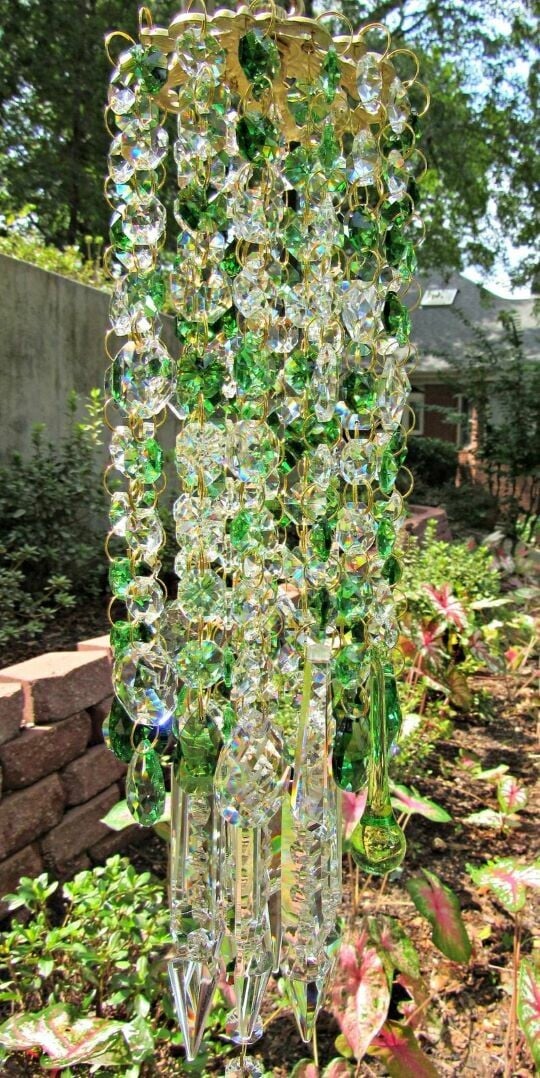 Green crystal wind chime detail hanging outdoors near foliage