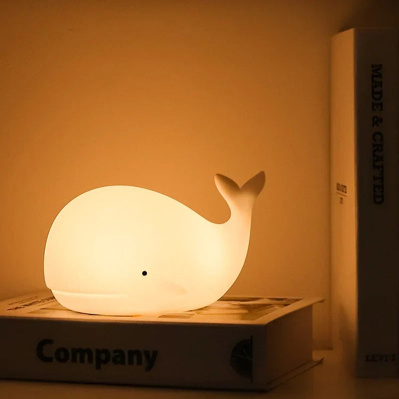 Cute whale night light glowing softly on a bedside table next to books
