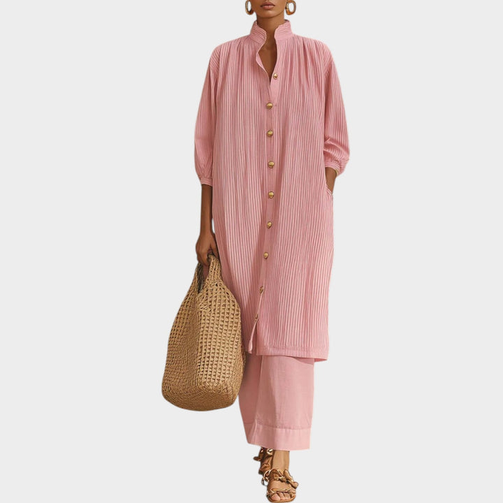 Front view of a woman wearing a pink button-down tunic and matching wide-leg pants holding a straw bag.