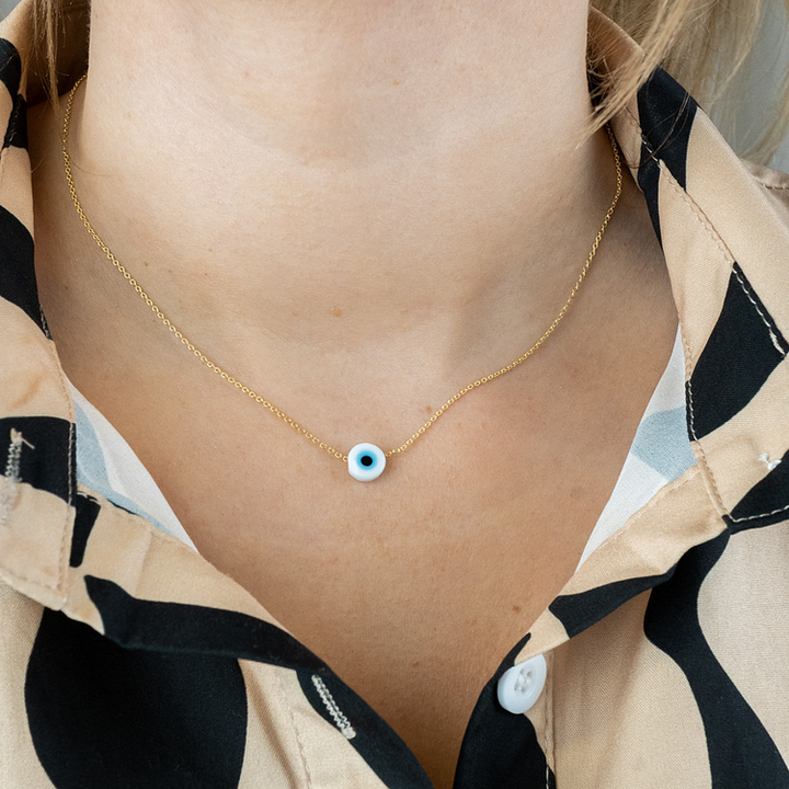 Model wearing a gold evil eye necklace with a white charm