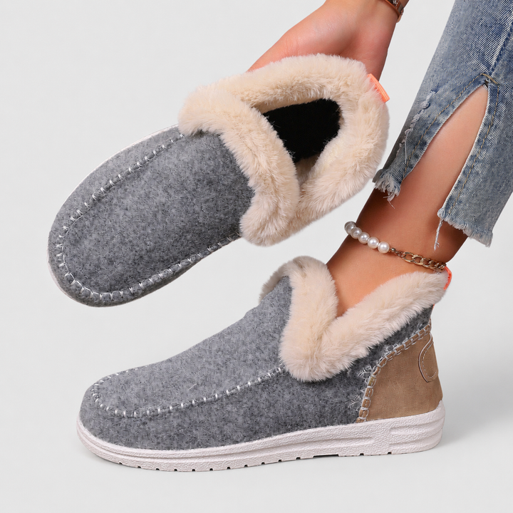 Close-up of women's grey fleece-lined house slippers held up showing the plush interior lining and textured sole.