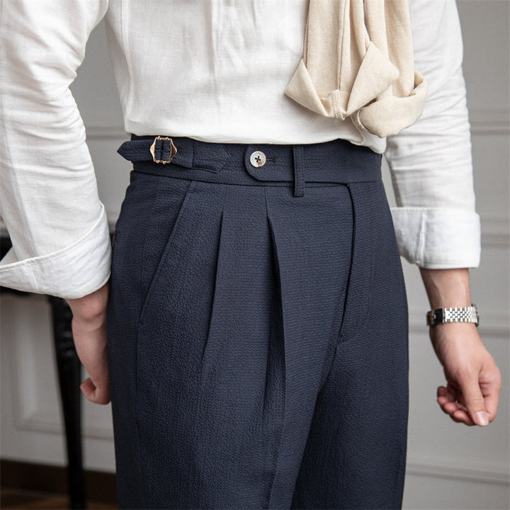 Close-up of navy blue pleated cropped trousers with side buckle detail and white shirt
