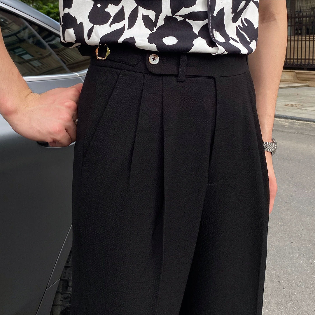 Close-up of black pleated cropped trousers with button closure and side adjusters
