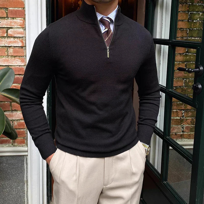 Man wearing a black quarter zip sweater with a striped tie and beige trousers