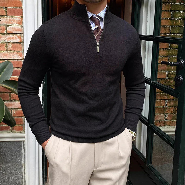 Man wearing a black quarter zip sweater with a striped tie and beige trousers