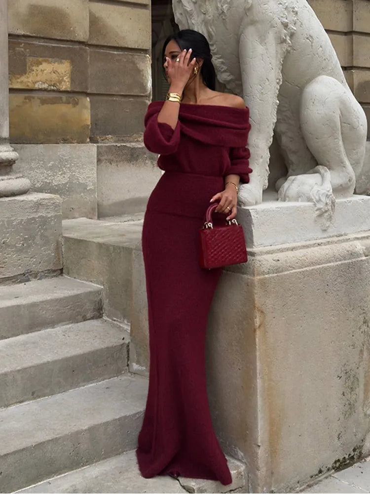 Full-length view of a woman posing against a stone wall in a red long-sleeve winter maxi dress