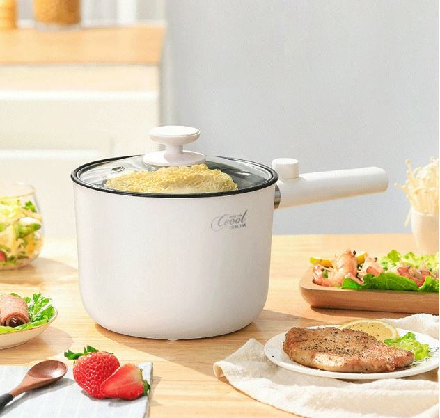 Compact white electric cooking pot with glass lid closed, placed on a dining table with side dishes.
