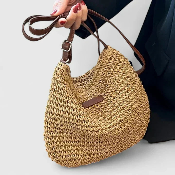 Close-up of a woven straw bag held by its adjustable brown strap
