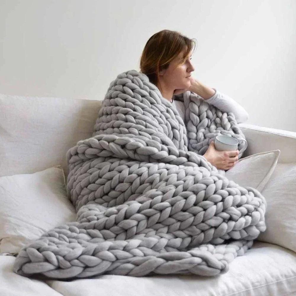 Woman wrapped in a light grey chunky knit blanket holding a mug