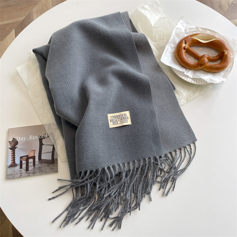 Gray reversible wrap scarf with fringe resting on a white table with a pretzel