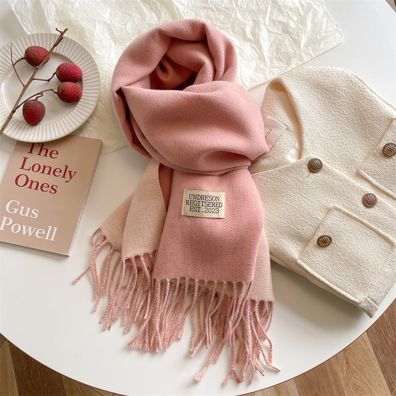 Pink reversible wrap scarf with fringe displayed near a plate of fruit and a book