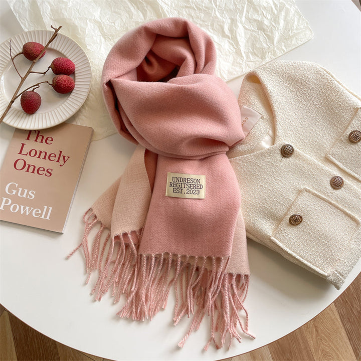 Pink reversible wrap scarf with fringe displayed near a plate of fruit and a book