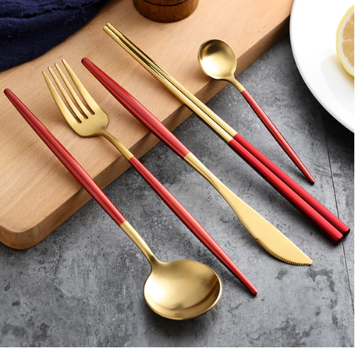 Close-up of a gold cutlery set featuring red handles arranged on a wooden board next to a white plate