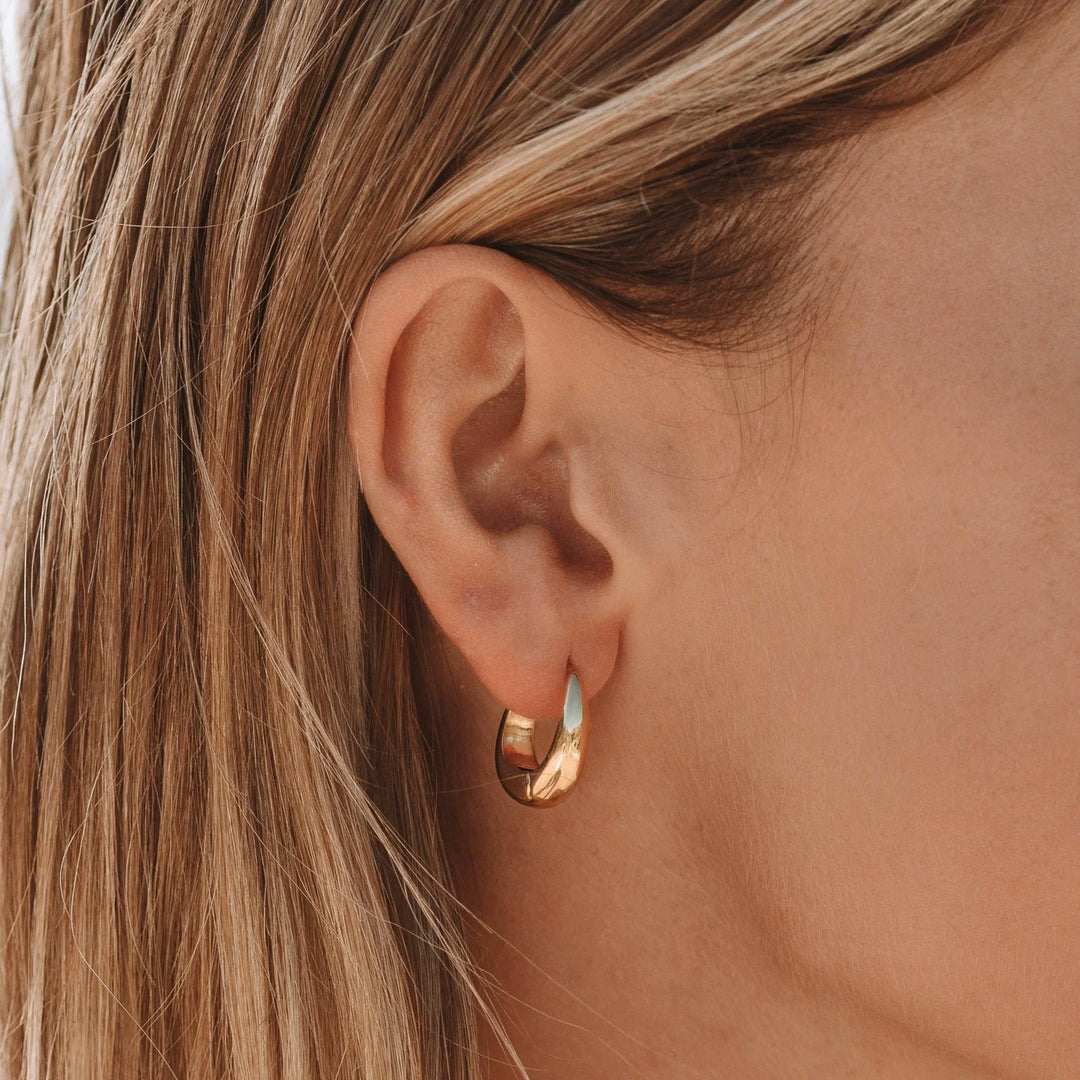 Close-up of a woman wearing gold Isla drop earrings in her earlobe