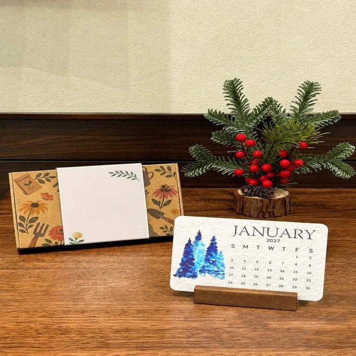 January card of the 2027 plantable seed paper calendar displayed on a wooden stand next to a pine tree decoration