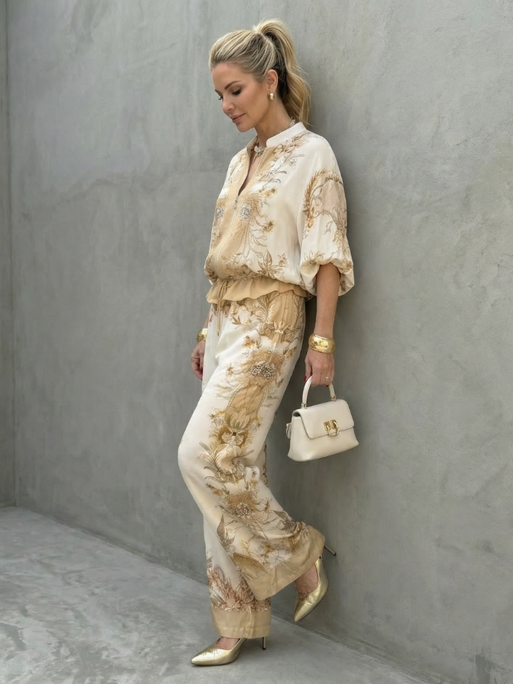 Side profile of a woman modeling the white and gold printed two-piece outfit against a grey wall