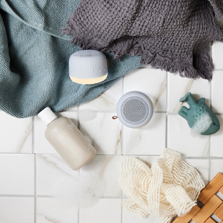 Two waterproof bathroom speakers placed on tiled surface with a towel and shower accessories
