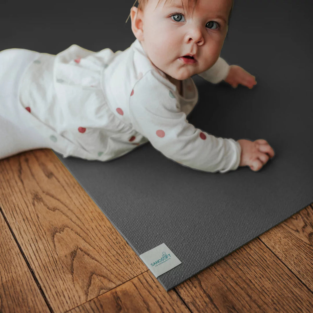 Baby crawling happily on a dark gray non-slip foam play mat placed on a wooden floor.