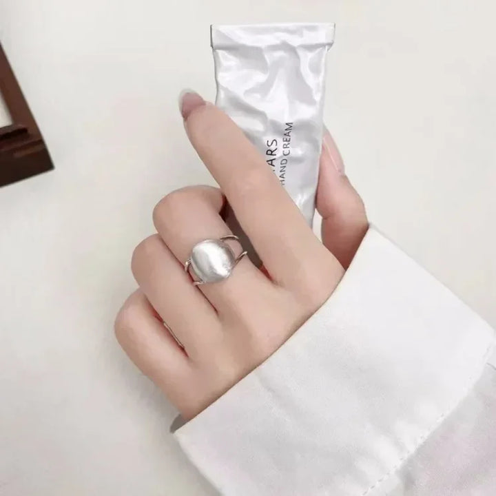 Hand wearing the silver sculptural ring while holding a hand cream tube