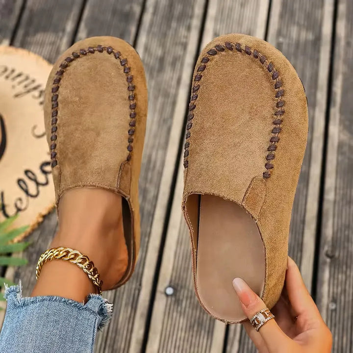 Women's brown slip-on flat orthopaedic sandals shown from above on a wooden background