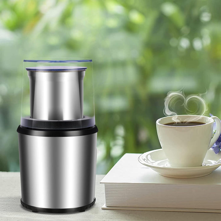 Stainless steel electric coffee grinder next to a cup of fresh coffee