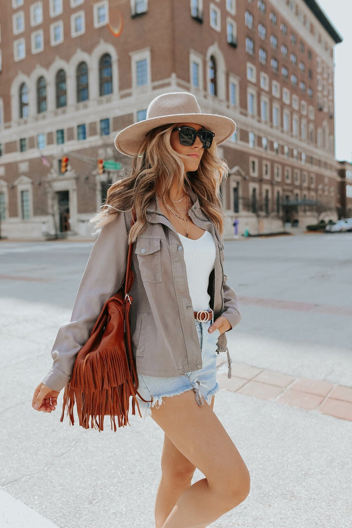 Side view of a woman wearing a casual jacket with a hat and fringe bag