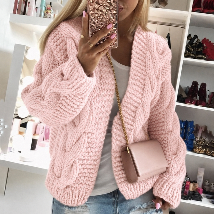 Woman wearing a pink oversized cable knit cardigan with long sleeves.