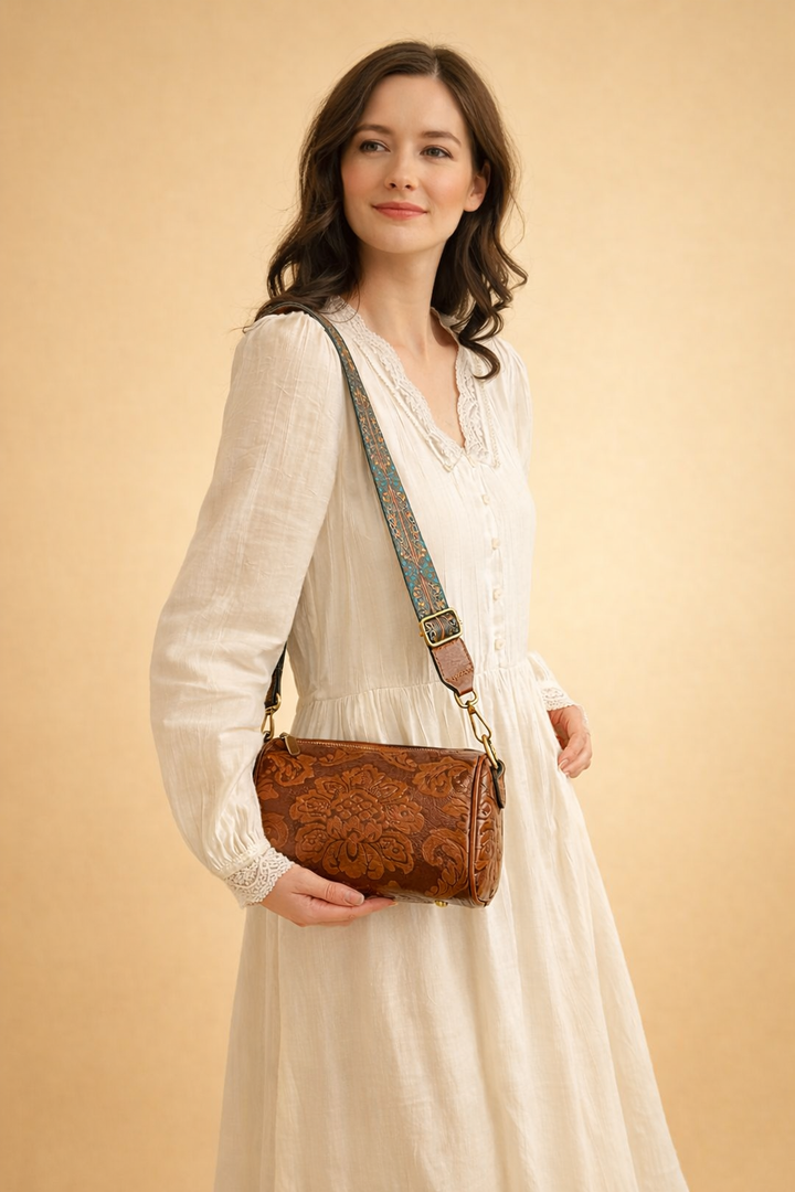 Model wearing a white dress and carrying the brown embossed cylinder crossbody bag