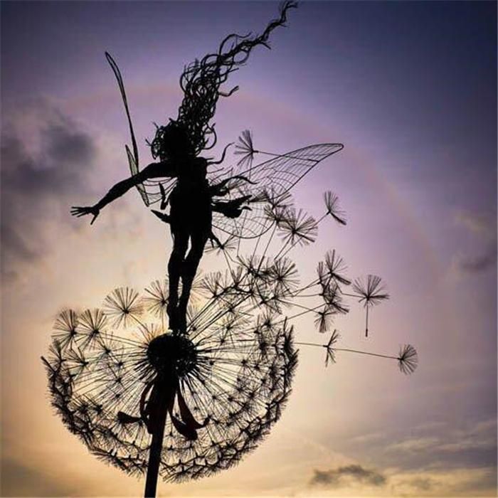 Silhouette of a metal fairy sculpture perched on a dandelion against a dusk sky