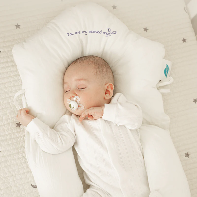 Baby sleeping peacefully on ergonomic white infant sleep support pillow in a crib