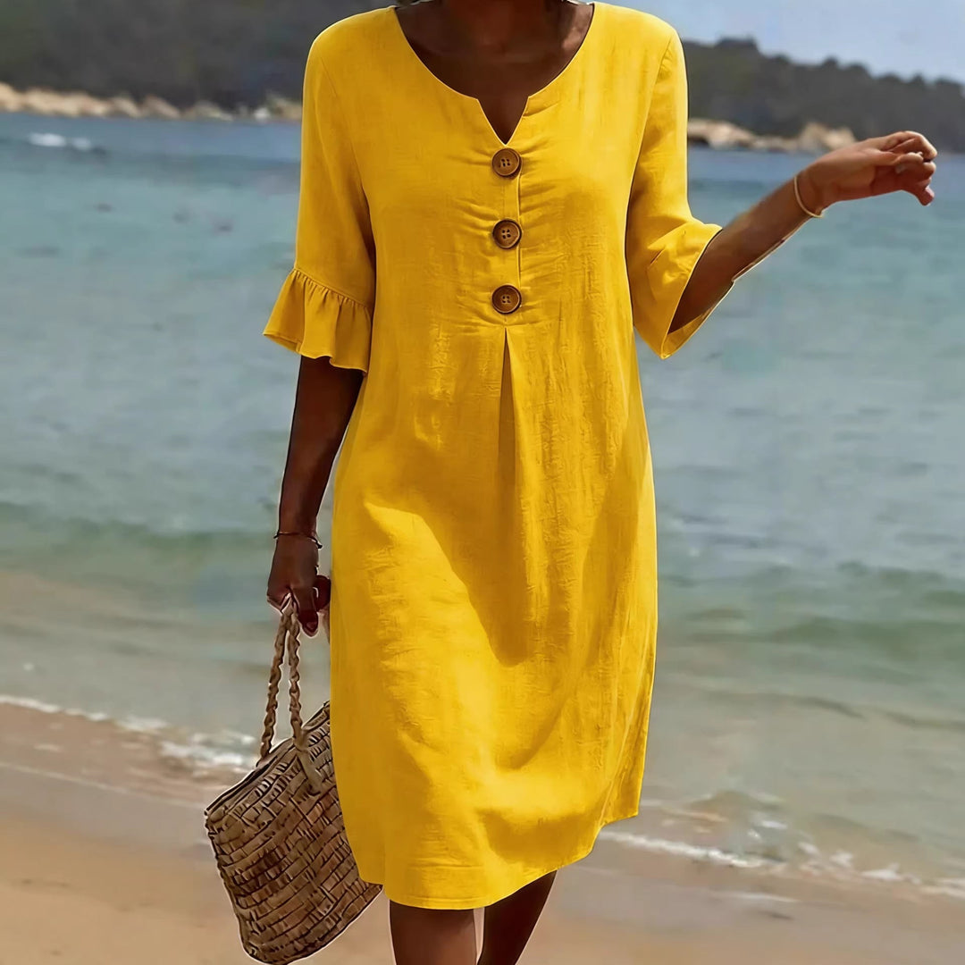 A woman walking on a sandy beach wearing a bright yellow V-neck mini dress.