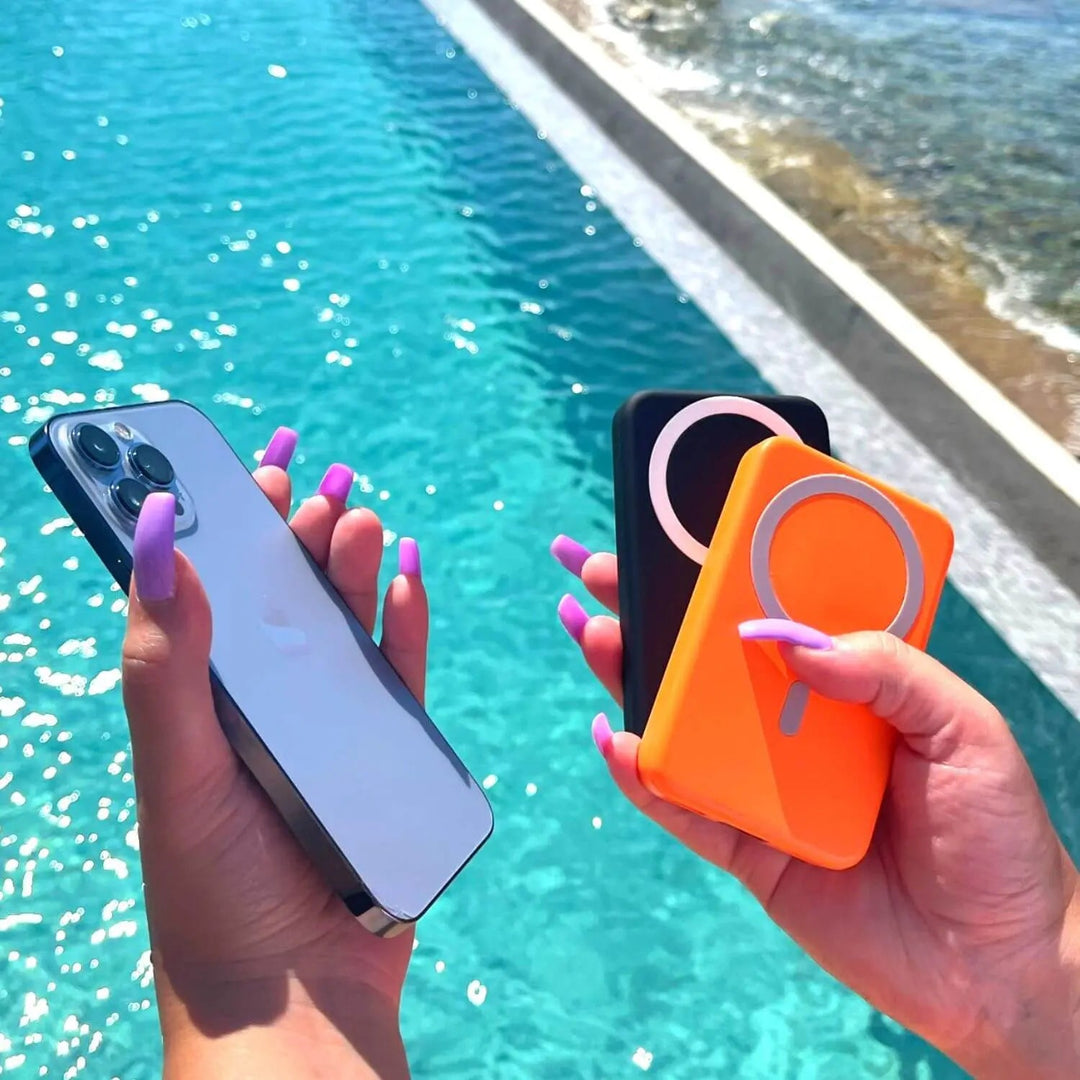 Hand holding colorful power banks near a swimming pool on a sunny day