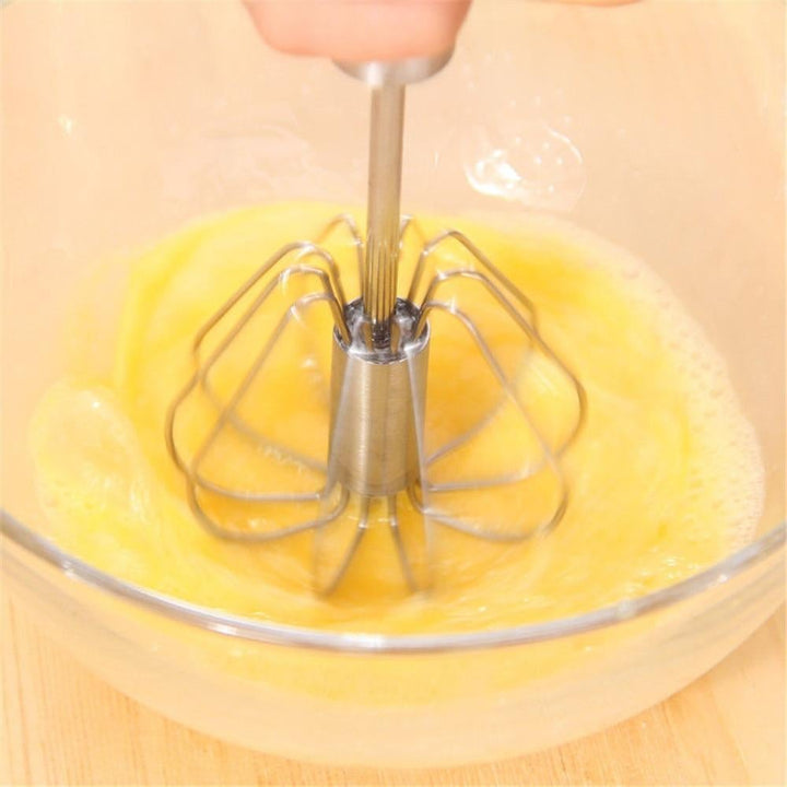 Hand pressing the stainless steel whisk into a bowl of egg mixture