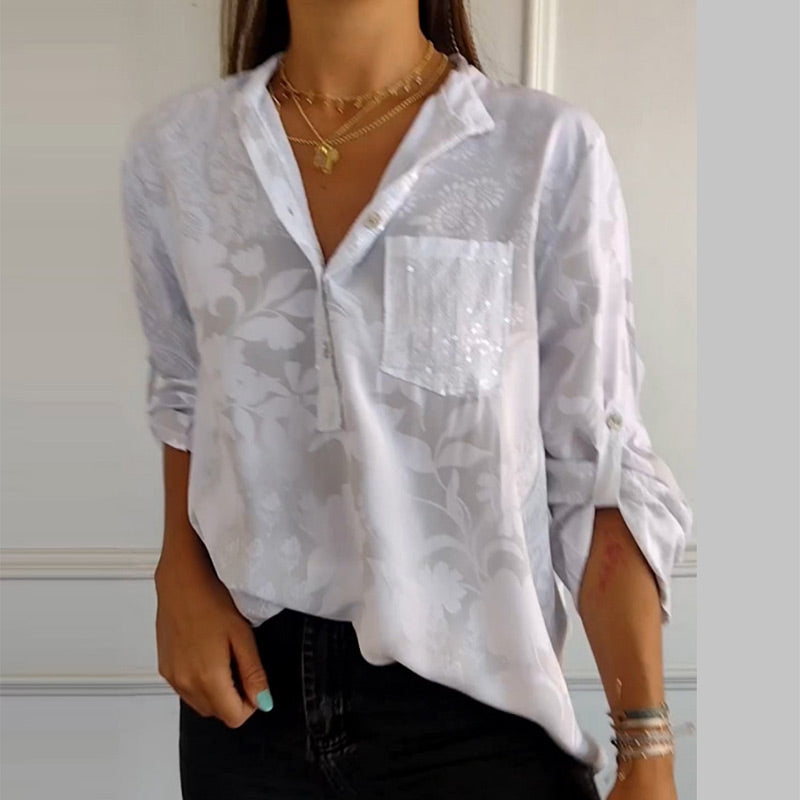 Model wearing a white V-neck button-down floral top paired with dark pants