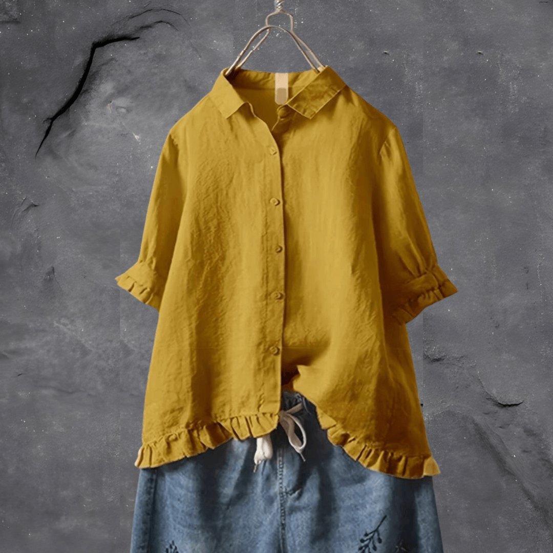 Yellow women's collared blouse with ruffle hem hanging against a textured wall