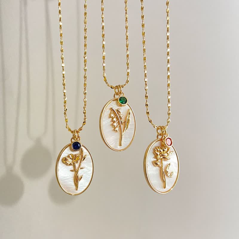 Three personalized birth flower and birthstone necklaces hanging vertically against a neutral wall