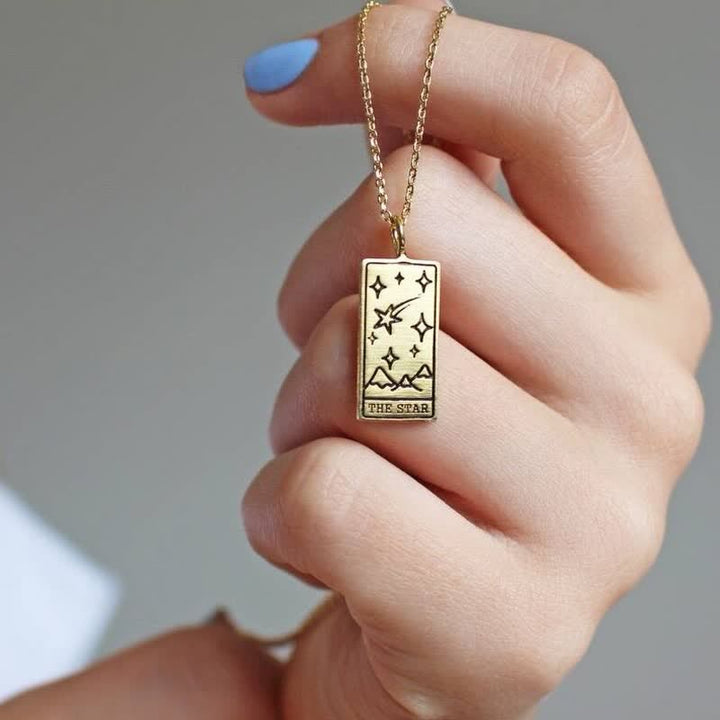 Close-up of a hand holding the Star tarot card pendant necklace in gold finish.