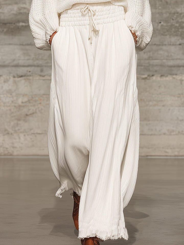 Close-up view of white wide-leg trousers with elastic waistband and drawstring detail.
