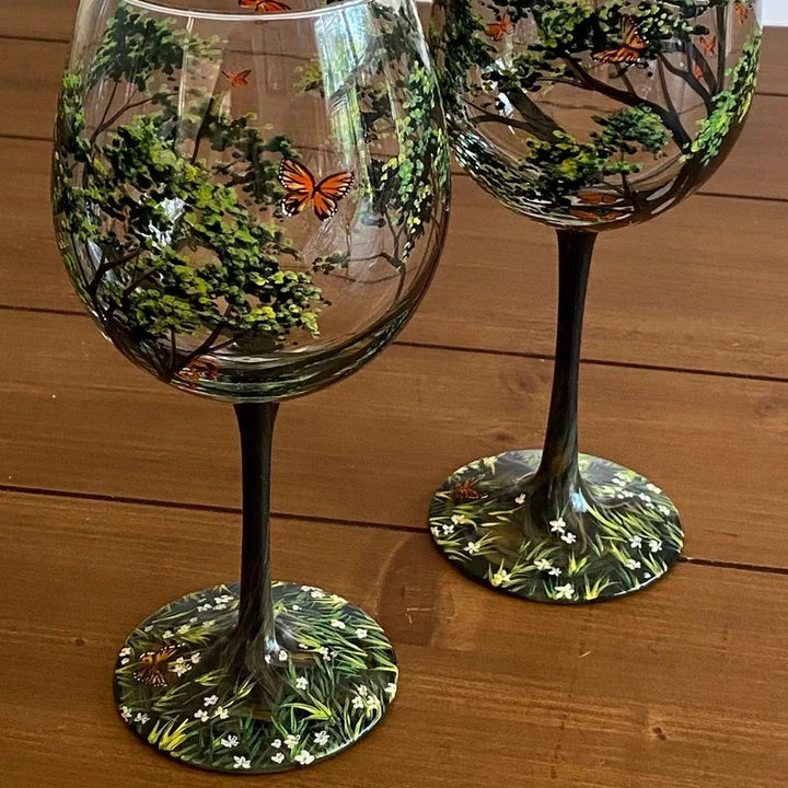Two hand-painted Spring tree wine glasses with stems on a wooden table