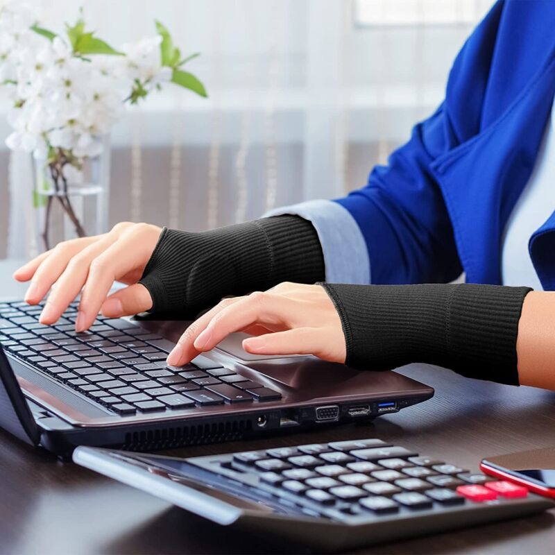 Person wearing black gel thumb support gloves while typing on a laptop computer
