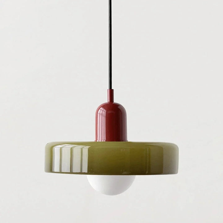 Modern glass pendant light with a red body and green lampshade hanging against a neutral background